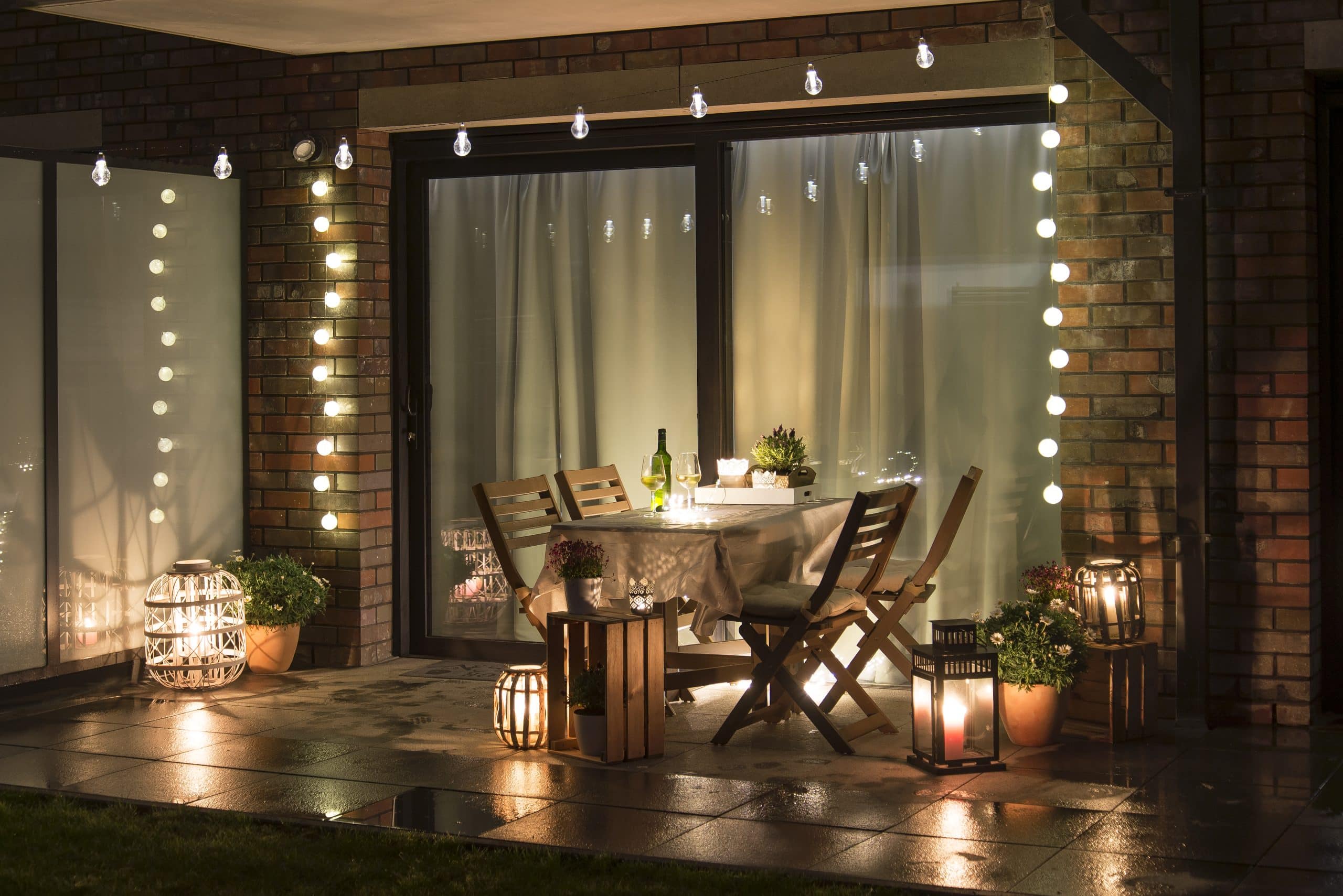 A patio in the summertime with fairy lights, lamps, and candles.