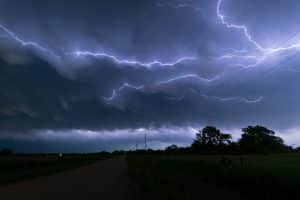A dark sky with a strike of lightning over a field with trees and powerlines.