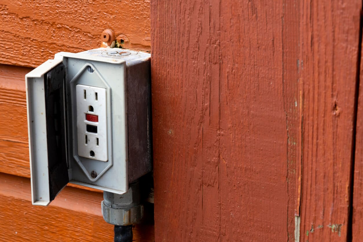 An outdoor electrical outlet on a wooden wall.