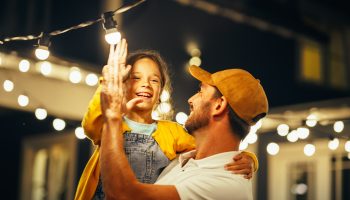 A Father Teaching His Daughter Electrical Safety As They Replace A Lightbulb On Outdoor Hanging Lights Together.