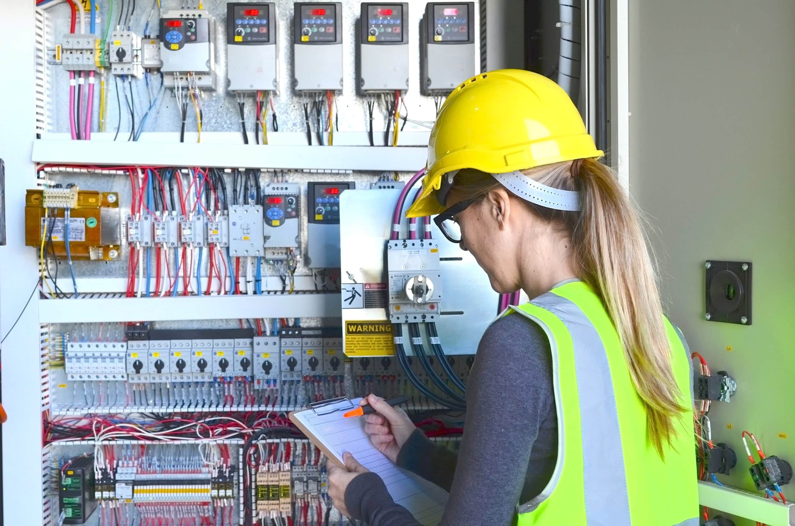 An electrician with a clipboard conducting an electrical inspection on an electrical panel.