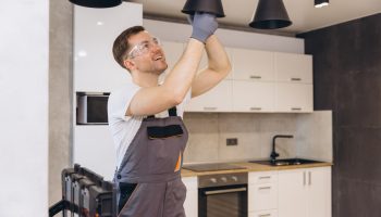 Electrician wearing safety glasses installs a black pendant light in a modern kitchen.