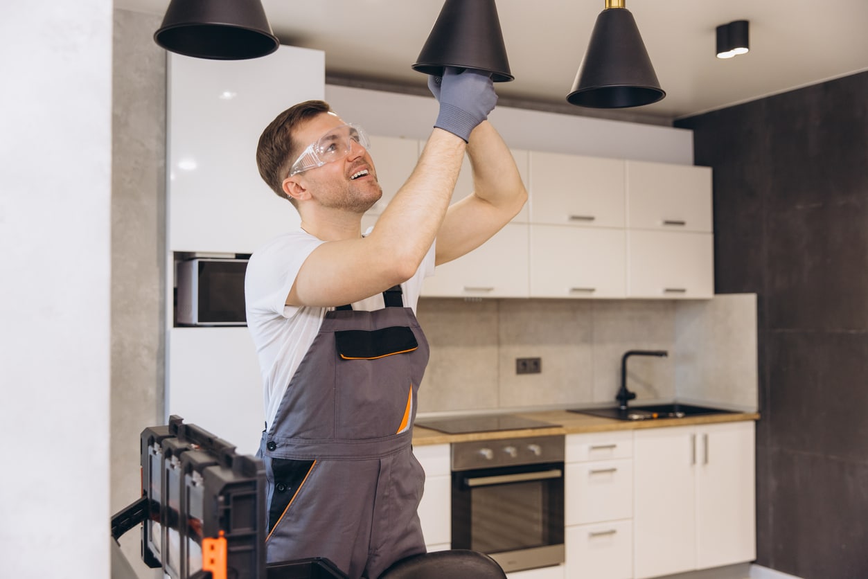 Electrician wearing safety glasses installs a black pendant light in a modern kitchen.