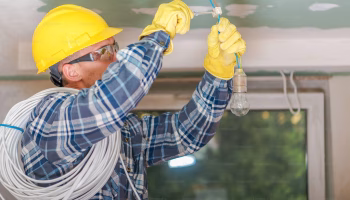 An electrician in a yellow safety hard hat works on a residential lighting system