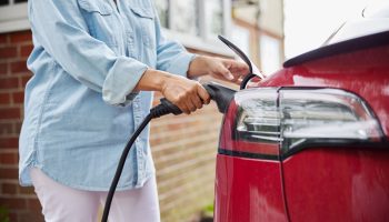 A woman charging her electric vehicle safely at home, highlighting the importance of preparation before EV charger installation.