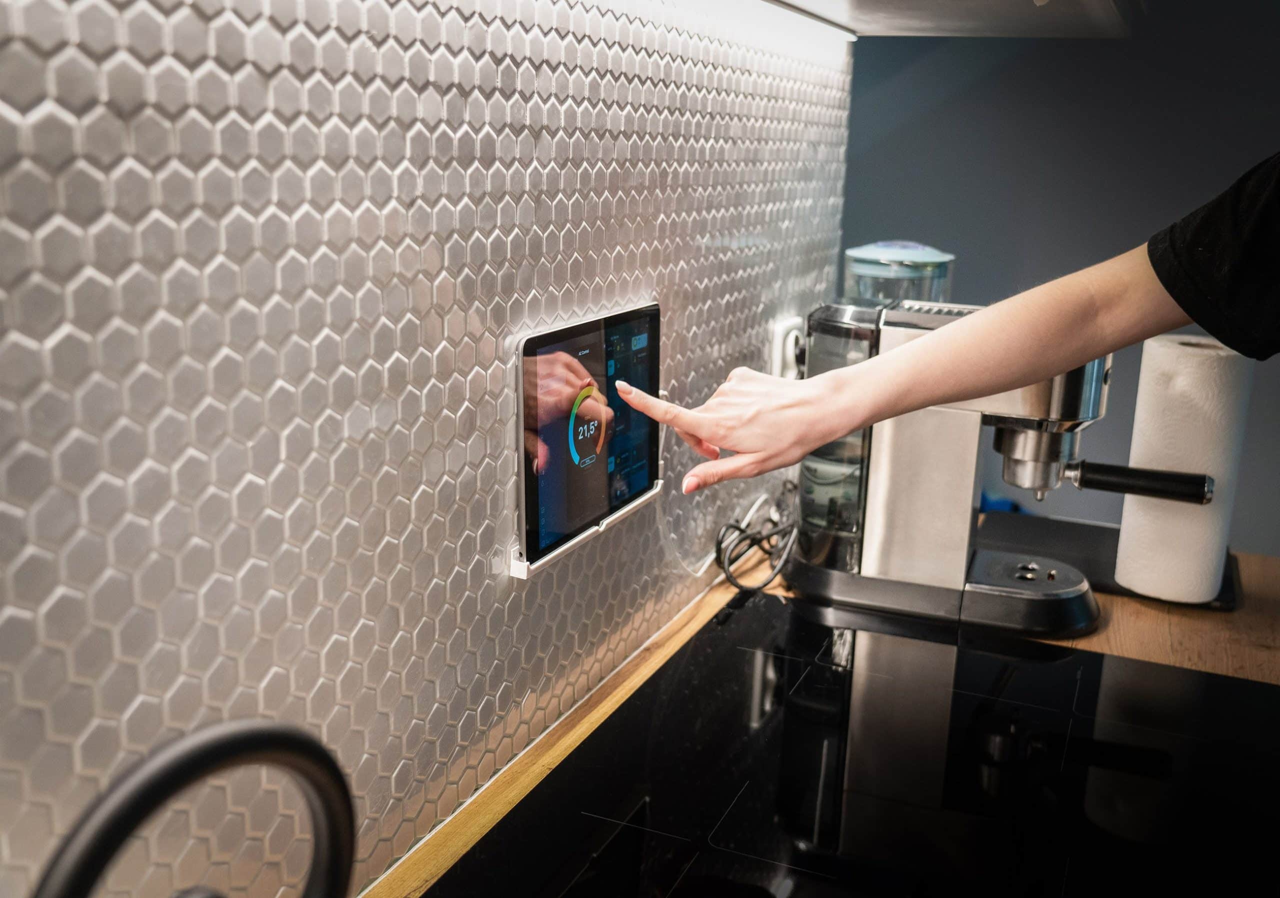Touchscreen smart home control panel mounted on a wall inside a modern home.