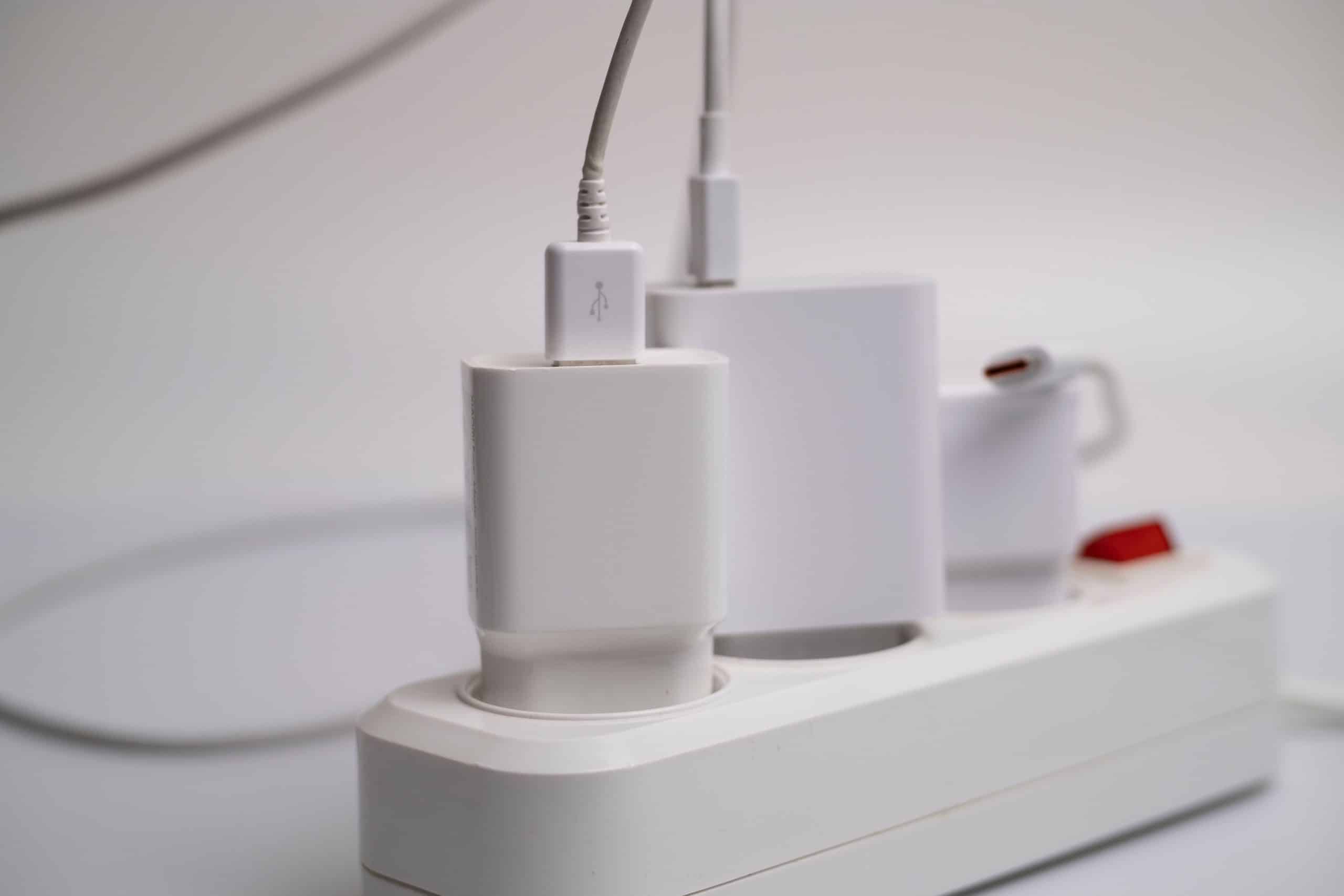 White power strip with several electrical plugs connected on a wooden floor.